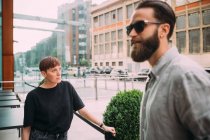 Bearded young man with brown hair wearing sunglasses and young woman with short hair standing outside a bar. — Stock Photo