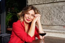 Ritratto di bella donna d'affari in giacca rossa con capelli biondi, vino rosso in vetro sul tavolo, guardando la macchina fotografica — Foto stock