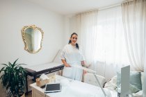 Beautician standing at treatment bed in beauty salon, smiling at camera. — Stock Photo