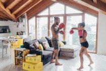 Homem tatuado barbudo com cabelos longos morena e mulher com cabelos longos marrom em pé dentro de casa, praticando kickboxing. — Fotografia de Stock