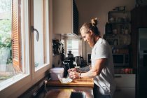 Barbu tatoué homme avec de longs cheveux bruns debout dans une cuisine, la préparation des aliments. — Photo de stock