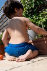 Rückansicht eines kleinen Jungen, der im Sommer in einem Garten kniet. — Stockfoto