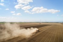 Trator soprando poeira no campo de batata seco nos Países Baixos, céu com nuvens — Fotografia de Stock