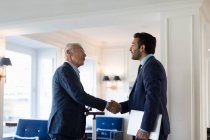 Two businessmen standing indoors, shaking hands. — Stock Photo