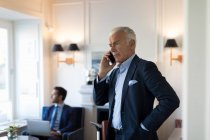 Senior businessman standing indoors, using mobile phone. — Stock Photo