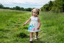 Portrait of young girl in white dress walking on a meadow, looking at camera. — Stock Photo