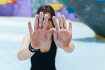 Woman in black outfit standing in front of indoor rock climbing wall, holding out chalk powdered hands. — Stock Photo