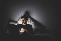 Бородатый молодой человек, лежащий в постели ночью, глядя на экран ноутбука — стоковое фото