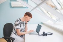Young woman with short hair sitting at desk, looking at laptop — Stock Photo