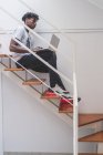 Молодий чоловік з короткими замками, що сидять на сходах, друкуючи на ноутбуці — стокове фото