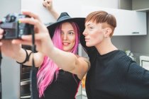Mujer joven con el pelo largo de color rosa y la mujer con el pelo corto de color rojo tomando cámara selfie - foto de stock