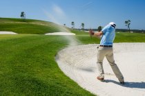 Golfista maschio scheggiando fuori trappola sabbia. — Foto stock
