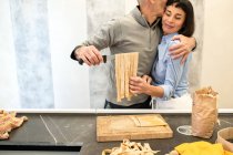 Couple standing in a kitchen, making fresh homemade tagliatelle pasta. — Stock Photo