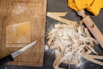 High angle close up of freshly made tagliatelle, rolling pin and knife on wooden cutting board. — Stock Photo
