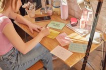 Chica adolescente sentada en su habitación en un escritorio, escribiendo citas motivacionales en tarjetas de notas. - foto de stock