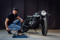 Молодий чоловічий мотоцикліст робить обслуговування на старовинному мотоциклі в гаражі — стокове фото