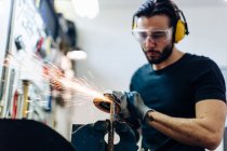 Young man using angle grinder on metal in workshop — Stock Photo