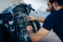 Jovem motociclista do sexo masculino reparar motocicleta vintage ao ar livre — Fotografia de Stock