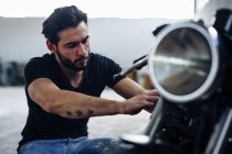 Young male motorcyclist repairing vintage motorcycle outdoors — Stock Photo