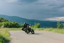 Joven motociclista masculino en motocicleta vintage girando alrededor de la curva de la carretera rural, Florencia, Toscana, Italia - foto de stock