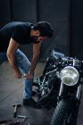 Young male motorcyclist repairing vintage motorcycle in garage — Stock Photo