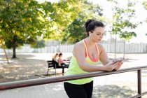 Жінка, використовуючи мобільний телефон в парку, друзі роблять перерву на задньому плані — стокове фото