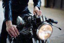 Young male motorcyclist straddling vintage motorcycle in garage, cropped — Stock Photo