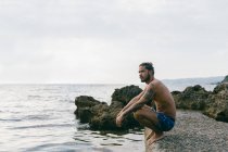 Чоловік сидить на пляжі біля водного краю — стокове фото