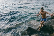 Чоловік стрибає з каменю на камінь у морі — стокове фото