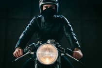 Молодий чоловічий мотоцикліст на старовинному мотоциклі в гаражі, портрет — стокове фото