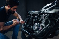 Young male motorcyclist repairing vintage motorcycle in garage — Stock Photo