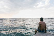 Чоловік сидить на краю моря — стокове фото