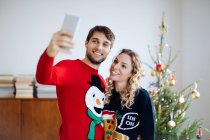 Casal tirando selfie na frente da árvore de Natal em casa — Fotografia de Stock