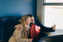 Пара, делающая селфи с шаром в форме сердца внутри поезда — стоковое фото
