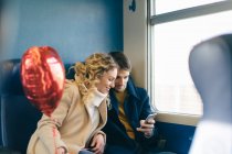 Casal com balão em forma de coração usando smartphone dentro do trem — Fotografia de Stock