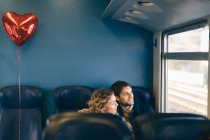 Couple with heart shaped balloon looking out window of train — Stock Photo