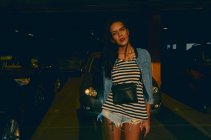 Portrait of woman with long brown hair, wearing hot pants, standing in car park at night. — Stock Photo