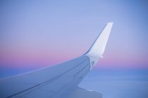 Vue le long de l'aile de l'avion de passagers volant au-dessus des nuages au coucher du soleil. — Photo de stock