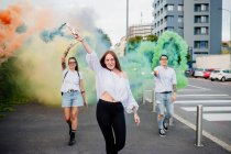 Смешанная расовая группа друзей тусуется вместе в городе, используя разноцветные дымовые шашки. — стоковое фото