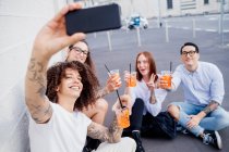 Grupo mixto de amigos pasando el rato juntos en la ciudad, tomando selfie con teléfono móvil. - foto de stock