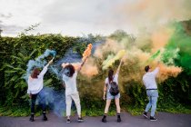 Grupo de amigos de raza mixta pasando el rato juntos en la ciudad, usando coloridas bombas de humo. - foto de stock