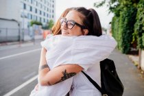 Two women with tattooed arms standing on sidewalk, hugging. — Stock Photo