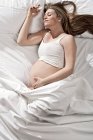 Retrato de una mujer muy embarazada acostada en la cama, con el estómago acunado. - foto de stock