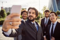 Mixed race group of businessmen hanging out together in town, taking selfie with mobile phone. — Stock Photo