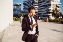 Retrato de empresário asiático vestindo terno escuro, verificando telefone celular. — Fotografia de Stock