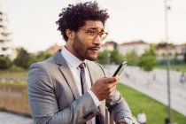 Retrato de empresário vestindo óculos e terno cinza, usando telefone celular. — Fotografia de Stock