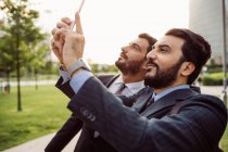 Два бізнесмени в костюмах, що стоять на відкритому повітрі, перевіряють свої мобільні телефони . — стокове фото