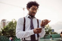 Retrato de empresário vestindo óculos, camisa branca, gravata marrom e suspensórios, ajustando suas algemas. — Fotografia de Stock