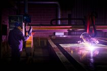 Hombre trabajando en una fábrica de acero, operando soldadora computarizada. - foto de stock