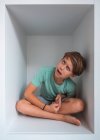 Portrait of brown haired boy sitting in closet, looking at camera. — Stock Photo